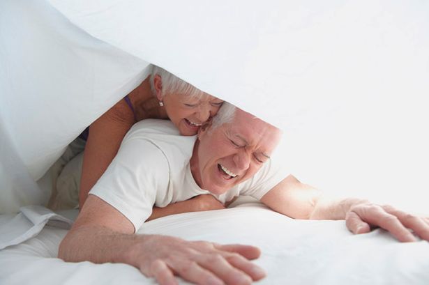 Elderly couple playing under sheet in bed